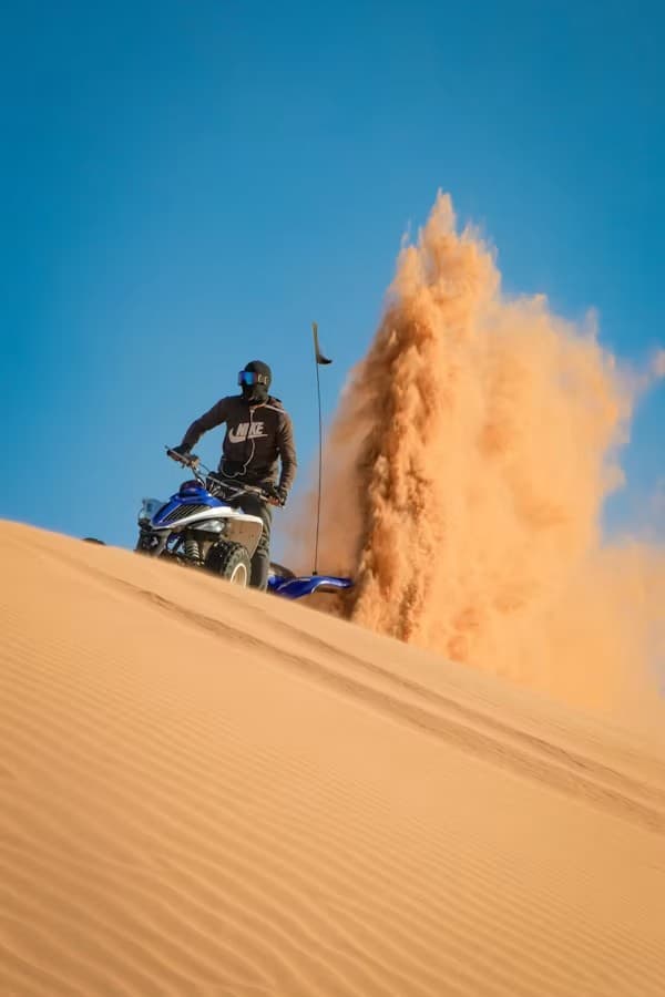 Pilote de quad dans les dunes près d'Essaouira, gerbe de sable orange